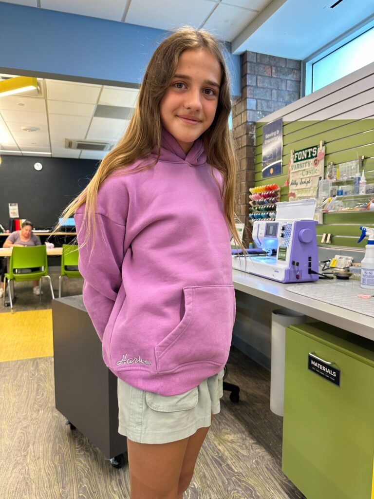 girl showing off her embroidered pink hoodie with her name